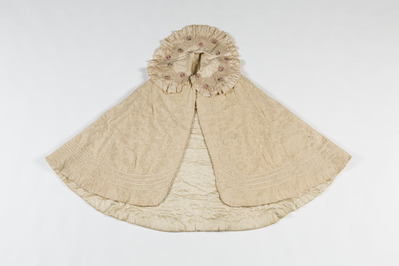 08390e99-2229-4efa-bf6c-222ec2d73745.jpg; 2013-0006-OWE; Cremekleurige, zijden gewatteerde mantel met goud bestikt en met bloemen bestikkte kraag; mantels (kleding)