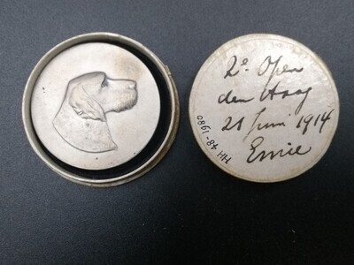 2194d55d-7d64-42d3-adc0-26eaff617efb.jpg; 1980-0048-HHI; Zilverkleurige prijspenning met hondekop in reliëf, tekst 'K.C.D.H. 21 juni 1914'.; onderscheidingen (eretitels)