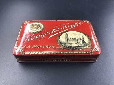 b4fd2a20-3b31-4673-b9c9-b02b044cb84c.jpg; 1981-0019-HHI; Blikken doos voor Haagse Hopjes met wapen van Den Haag en afbeelding van het Vredespaleis. Rood gekleurd met gouden detailleringen.; blikken (houders)